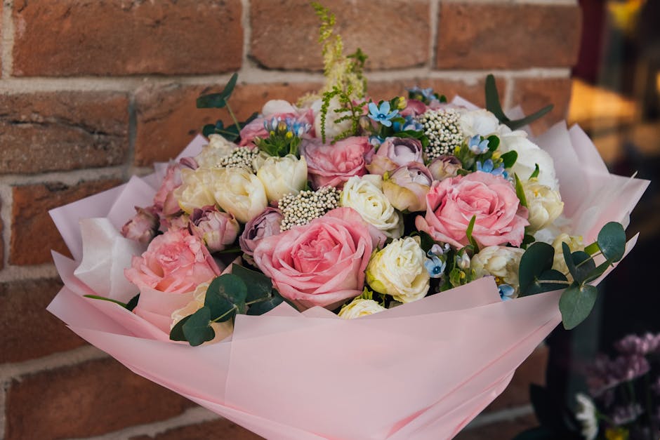 A bouquet of fresh flowers arranged in a rounded style, featuring large pink roses, creamy white lisianthus, and small blue forget-me-nots, accented with white baby's breath and green eucalyptus leave